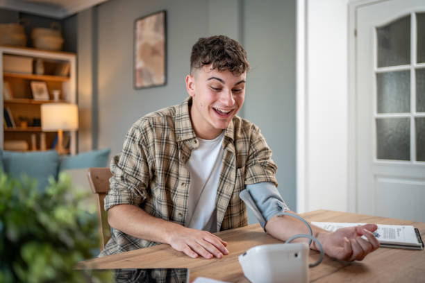 a young student measures his blood pressure, checks his health and the amount of stress while studying for an exam - blood pressure gauge medical exam healthcare and medicine equipment foto e immagini stock