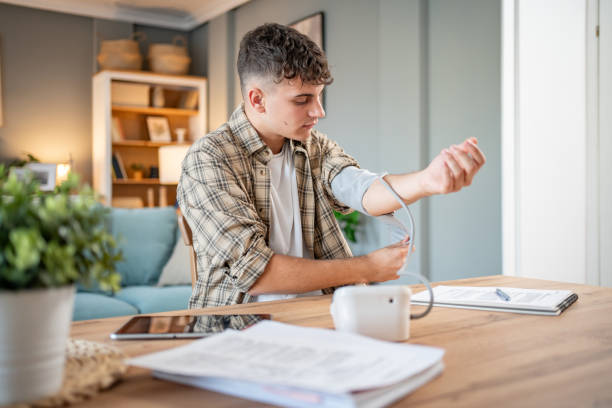 a young student measures his blood pressure, checks his health and the amount of stress while studying for an exam - blood pressure gauge medical exam healthcare and medicine equipment foto e immagini stock