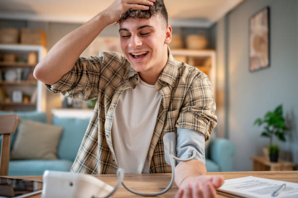 a young student measures his blood pressure, checks his health and the amount of stress while studying for an exam - blood pressure gauge medical exam healthcare and medicine equipment foto e immagini stock