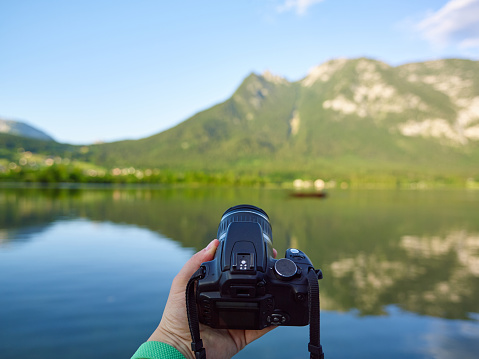 A man is holding a branded dslr camera with one hand and wants to take a photo of the mountains