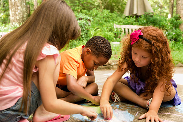 bambini: gruppo multi-etnico giocando con gesso sulla strada. - little girls sidewalk child chalk foto e immagini stock