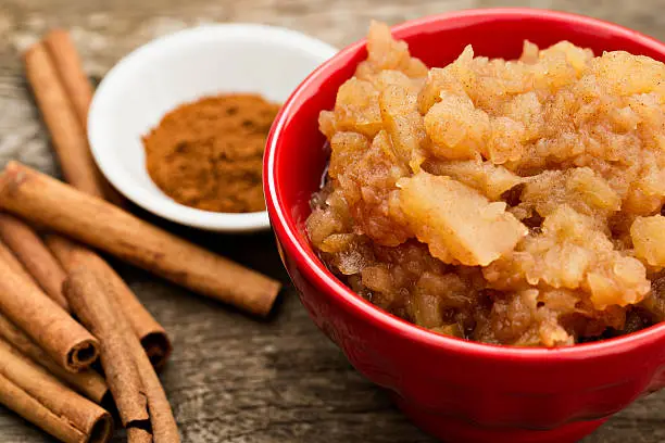 An overhead close up shot of a bowl of homemade apple sauce and cinnamon.