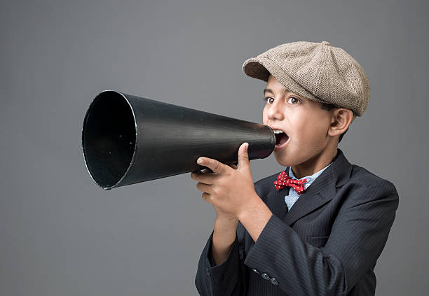 istock Little boy with newsboy cap shouting on old fashioned megaphone 187342829