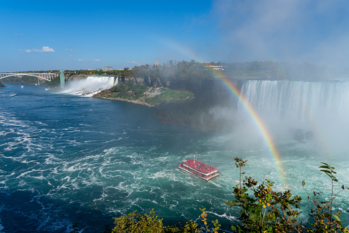 Beautiful landscape photo of white splash water fall at Cave of the wind Niagara Falls with birds seagull flying over, colorful rainbow with yacht on the water background, summer time in USA.