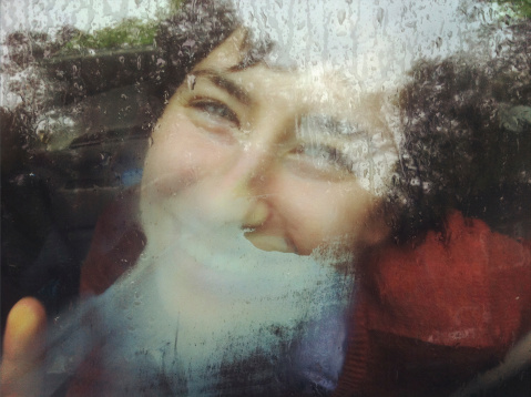 happy young woman smiling and laughing, her breath has fogged the wet car window