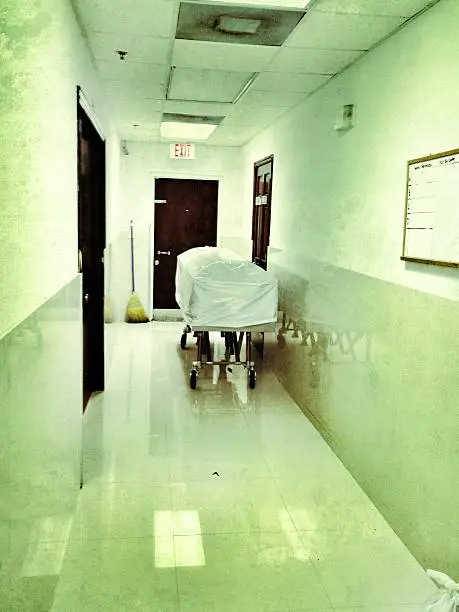 Morgue hallway with a wrapped up coffin on a gurney.