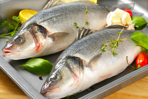 detail of two fresh sea basses with garnish on baking tin
