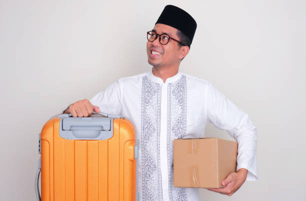 istock Moslem Asian man smiling and looking to upper right corner while carrying suitcase and package box 1873472256