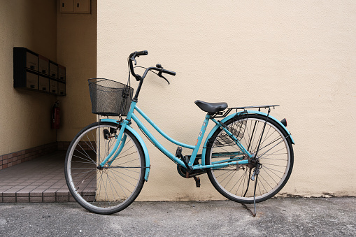 Old blue bicycle with metal basket parked beside a beige wall.