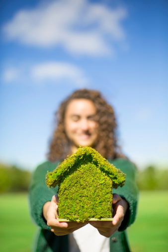 Happy woman holding organic moss covered house. Focus on house. 