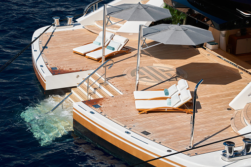 Close-up view of a relaxation area on the open teak deck on the stern of an expensive huge mega yacht at sunny day, stairs to water, wealth life, lounge chairs. High quality photo