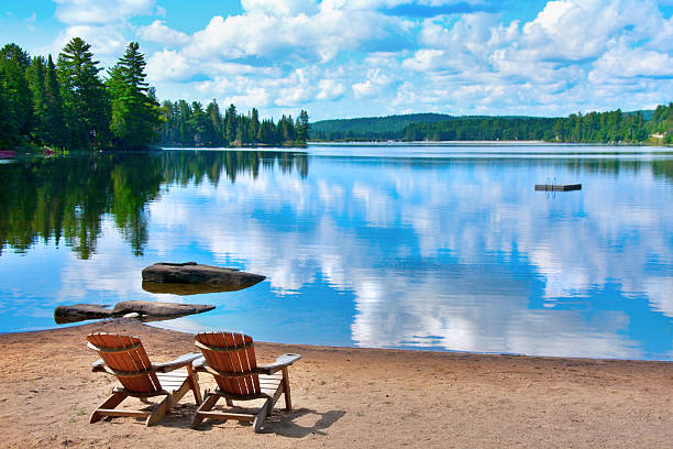 chairs lake shore two wooden deck chairs on the shore of a lake in Canada with clouds reflecting on the water ontario canada stock pictures, royalty-free photos & images