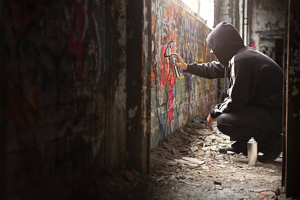 Illegal Young man Spraying black paint on a Graffiti wall. stock photo