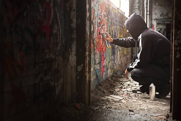 Illegal Young man Spraying black paint on a Graffiti wall. Illegal Young man Spraying black paint on a Graffiti wall. (room for text) child crimes stock pictures, royalty-free photos & images