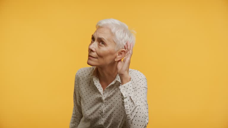 Senior Woman Listening Intently on Yellow