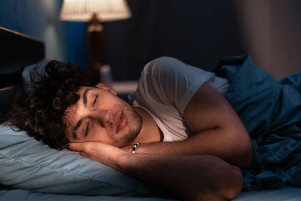 istock Handsome man sleeping in his cozy bed at night. Attractive guy sleeping profoundly and dreaming at home with blue light. Muslim man asleep with closed eyes. 1873559513