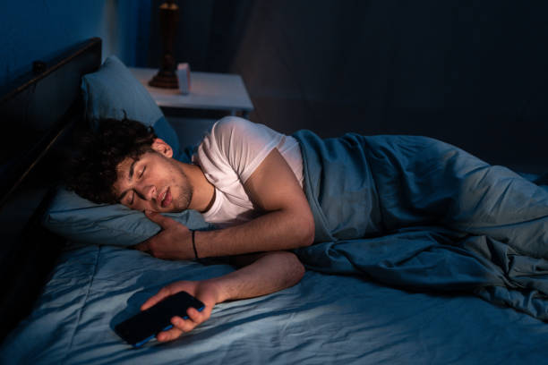 istock Arabic male lying on comfortable pillow with cellphone in hand and sleeping under blanket at night. Addiction and insomnia 1873559518