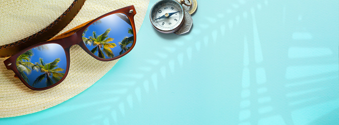 concept vacation and summer travel banner. Happy holidays on tropical sea beach. Panama hat, compass, sunglasses with a reflection of the sandy trovic beach and palm trees