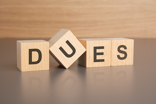 four wooden cubes with the letters DUES on the bright surface of a brown table. the inscription on the cubes is reflected from the surface of the table. business concept.