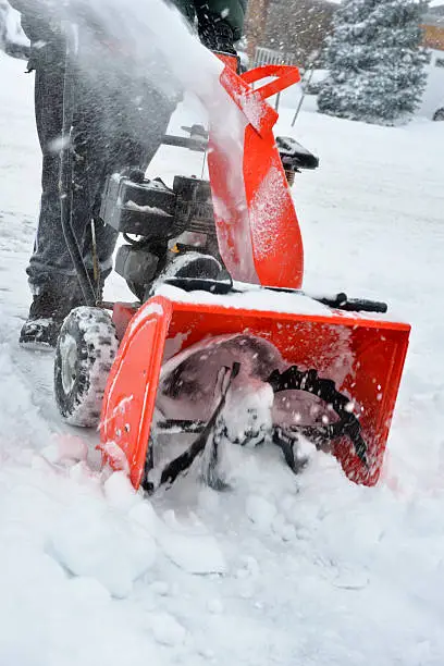 man using snowblower to clear snow on a driveway