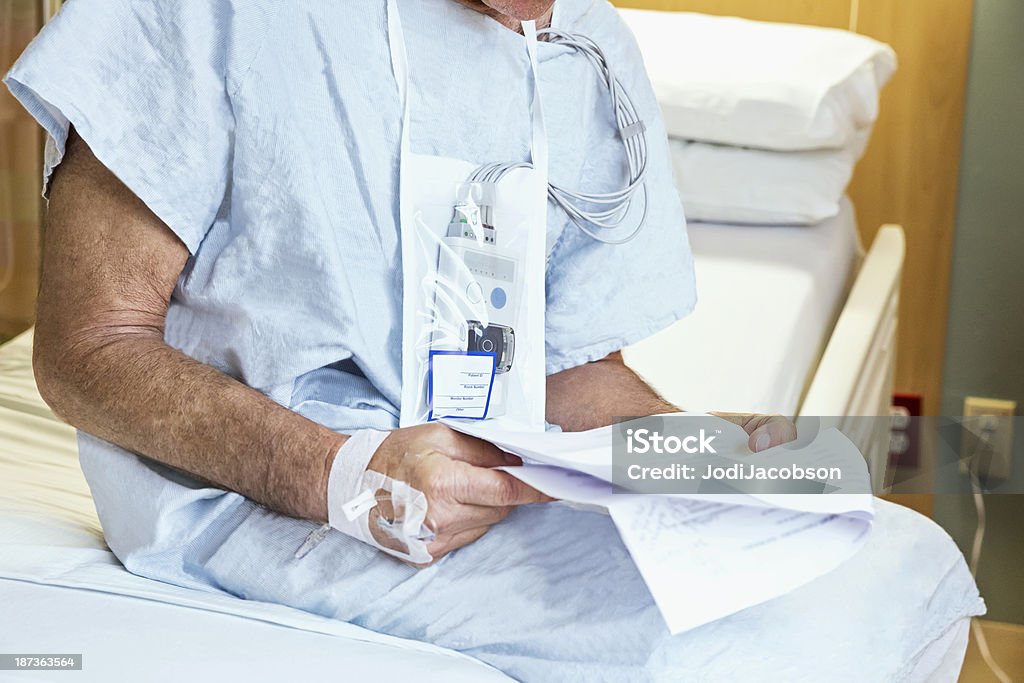 Homem sênior situa-se em sua cama lendo informações quarto de hospital - Foto de stock de Adulto royalty-free