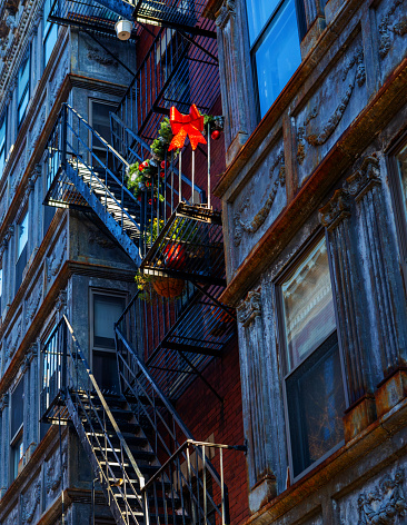 Boston, Massachusetts, USA - December 20, 2023: A red bow, red Christmas ball ornaments, and green plants decorate a fire escape on the side of a very old resdential building.