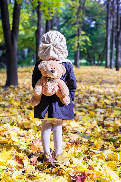 istock Little girl with backpack-bear behind in the autumn sunny forest 187372437
