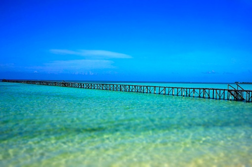This photograph showcases a long wooden pier stretching across the shallow turquoise waters of a tranquil sea under a vast blue sky in Virgin Gorda.