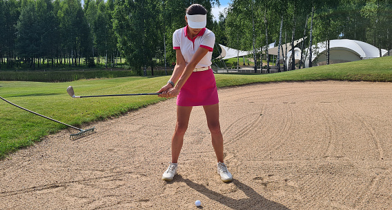 Female golfer in action swinging in sand pit during practice before golf tournament on golf course concept
