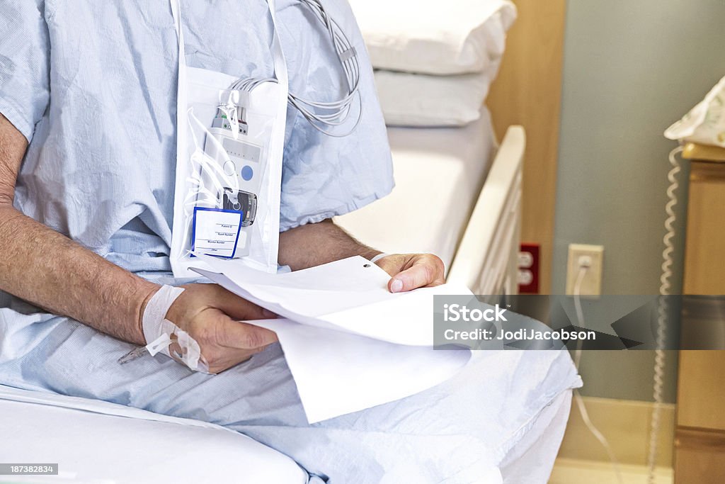 Uomo anziano si trova sul suo letto di ospedale lettura delle informazioni - Foto stock royalty-free di Adulto