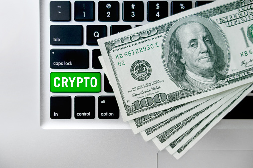 Close up laptop enter button   with “Cryptocurrency” text  with 100 dollar bills