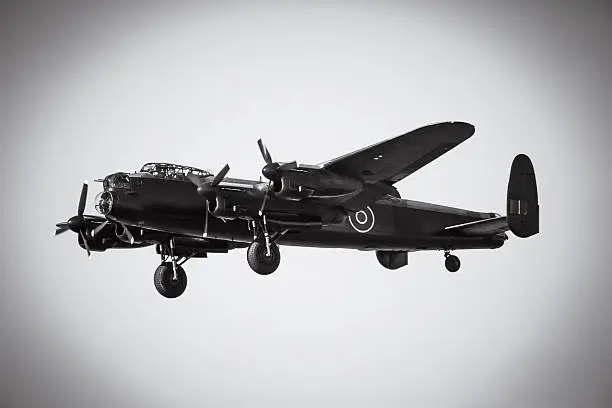 An aged image of an Avro Lancaster in flight with wheels down forlanding.  Black and white photo with vignette for ageing effect.  Made famous for the Dambuster raid on the Ruhr Valley by 617 Squadron of Air Marshal Sir Arthur Harris's RAF Bomber Command, commanded by Wing Commander Guy Gibson.  1943.  Flying from right to left with a clear sky in the background.