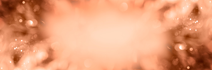 Festive shiny background with tinsel bokeh. Blurred background of peach fuzz. Web-banner