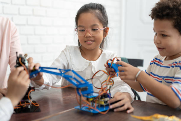 教室で電気ロボットと友人と勉強している幸せなアジアの子供の女の子 - child group of people multi ethnic group classroom ストックフォトと画像