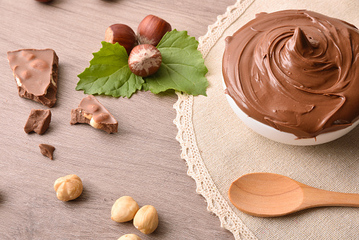 Milk chocolate and hazelnut cream on brown tablecloth on wooden table with leaves and nuts. Elevated view.