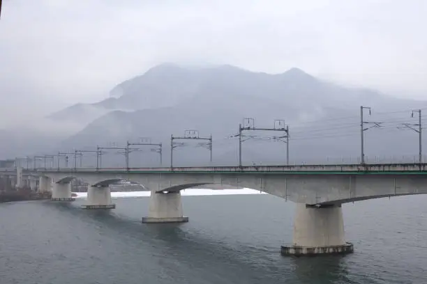 Yangpyeong County, South Korea - February 15, 2020: Amidst winter's embrace, the modernized Yangsu Railway Bridge stands over the North Han River, with foggy mountains and Korail's electric trains.