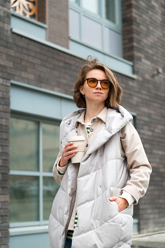 Young woman wearing glasses holding coffee cup portrait at city street. High quality photo