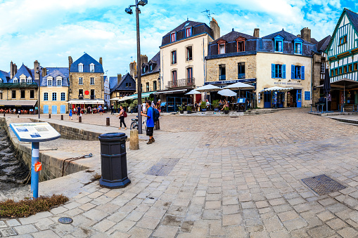 Captured in this photograph is the picturesque harbor of Port Saint-Goustan, where the timeless beauty of Brittany unfolds in a scene of maritime charm. The quayside, lined with historic buildings and bustling with activity, exudes an enchanting atmosphere that transports visitors to a bygone era.\n\nTraditional Breton architecture, with its colorful facades and half-timbered structures, frames the waterfront, creating a postcard-worthy scene. Moored boats gently bob in the calm waters, their reflections adding a tranquil allure to the harbor's ambiance. Cobblestone streets wind their way along the water's edge, inviting leisurely strolls and providing a perfect vantage point for absorbing the maritime panorama.\n\nThe play of sunlight on the water enhances the vibrant hues of the boats and buildings, casting a warm glow that accentuates the coastal allure. Quaint cafés and seafood eateries line the waterfront, inviting visitors to savor the maritime atmosphere and indulge in the delights of Breton cuisine. This image encapsulates the essence of Port Saint-Goustan, a timeless harbor where history, maritime culture, and natural beauty converge in a captivating tableau.