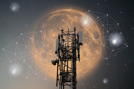 Mobile phone mast in the night sky in front of a bright blood moon. Network structure with docking points symbolizes the global network.