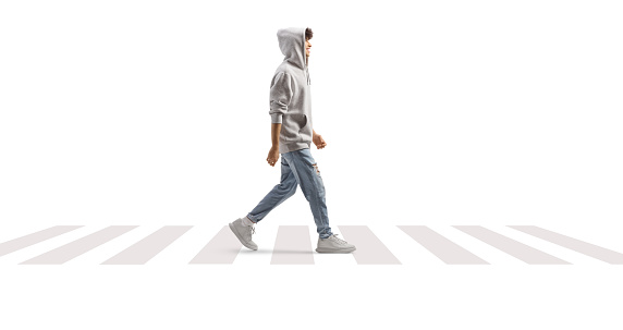 Full length shot of a guy wearing a gray hoodie and walking at a pedestrian crossing isolated on white background