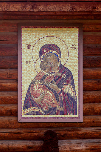 Icon of Our Lady hanging on the log wall of a wooden church.
