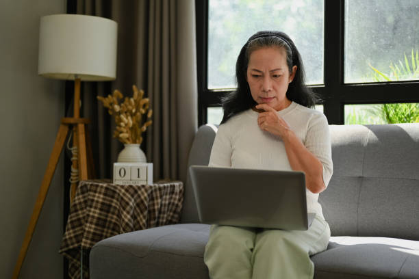 istock Happy middle age lady checking email or working on laptop while relaxing on the couch at home. 1874143035