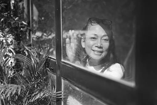 Black and white portrait of happy senior woman near window and l looking in distance dreaming or visualizing