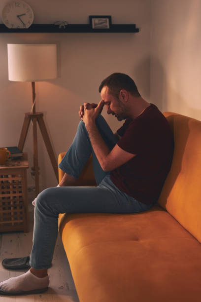 istock Man with headache and knee pain sitting on a sofa at home. 1874168065