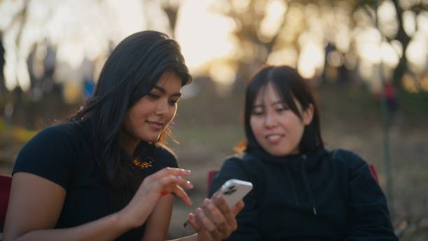 istock Two multi-ethnic women friends using mobile smart phone in nature 1874198495