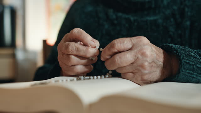 SLO MO Closeup Midsection of Senior Woman Counting Rosary Beads while Reading Holy Bible at Table at Home