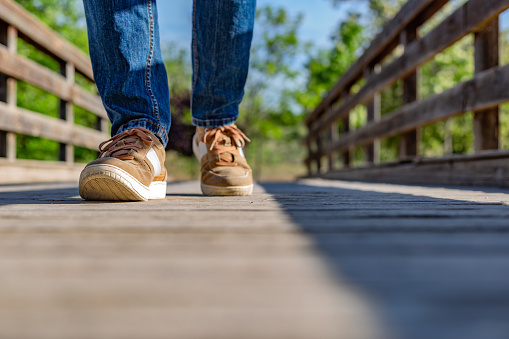Madrid, Spain. Partial view of a man's legs in jeans and sneakers walking on a wooden bridge in a natural park.
