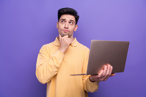 Photo of suspicious uncertain man dressed yellow shirt working modern device looking empty space hand arm chin isolated purple color background.