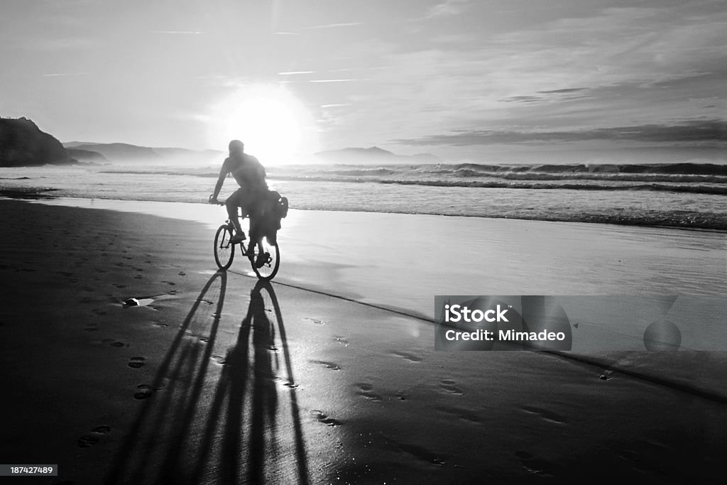 biker biking on beach at sunset with bicycle shadow biker biking on beach at sunset with bicycle shadow in black and white Bicycle Stock Photo
