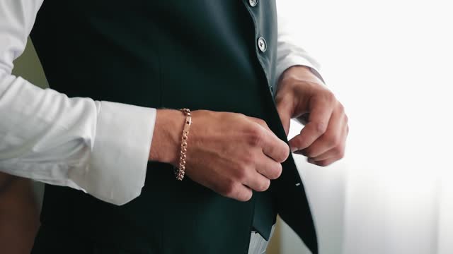 Male hands fasten a button on a jacket. Close up. The groom fastens his jacket with his hands. A stylish man in a suit fastens his buttons, getting ready to go out.